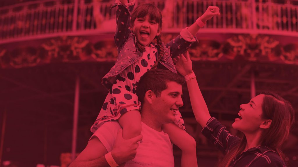 Happy smiling child sitting on the shoulders of her father with the mother smiling too.